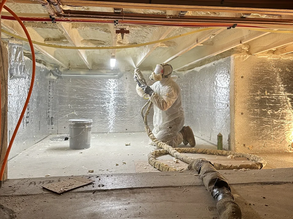 Professional installer applying spray foam insulation in a building crawlspace